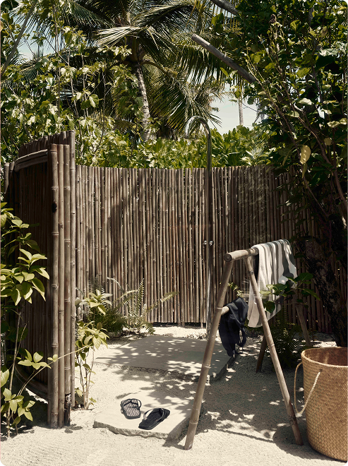 Bamboo-enclosed outdoor shower with sand floor.