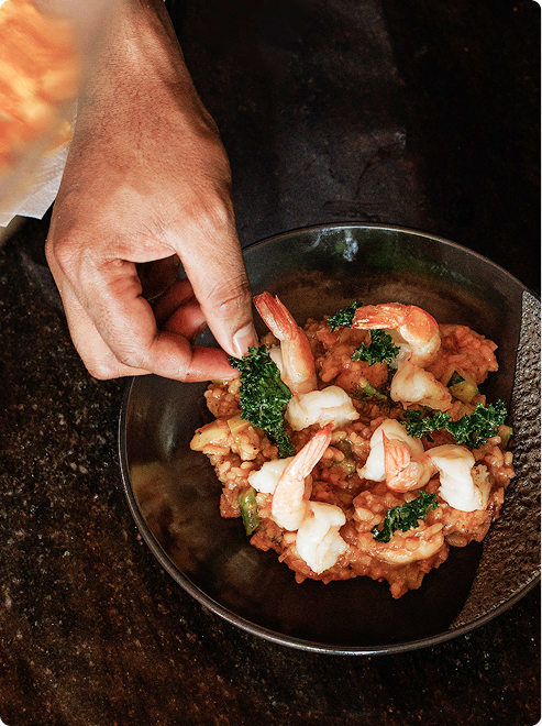 Hand garnishing shrimp risotto in bowl.
