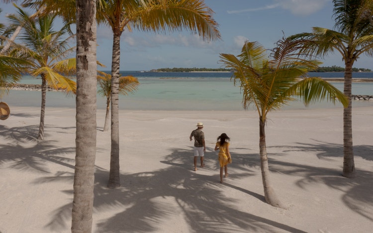 Couple walks toward turquoise ocean horizon.
