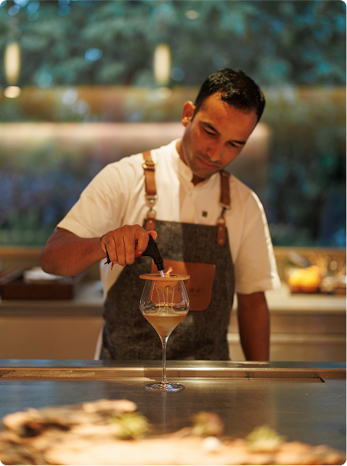 Bartender smokes creamy drink with wood.