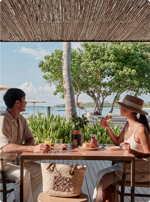 Couple enjoys croissants under thatched shade.