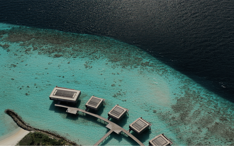 Overwater villas curve above coral reef.