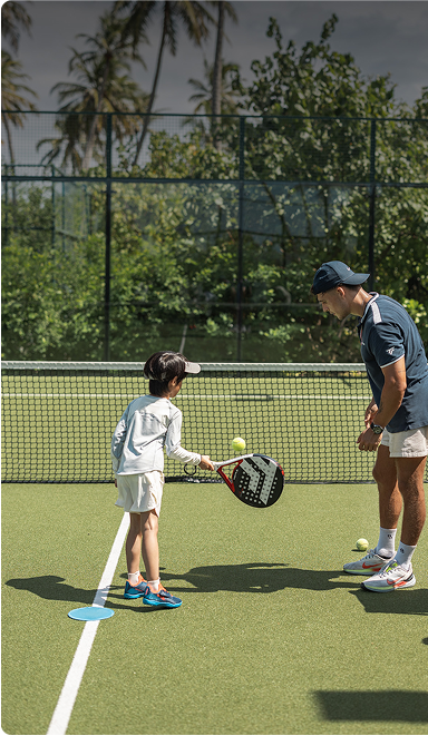 Coach guides child on tennis technique.