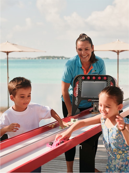 Children race toy cars outdoors.