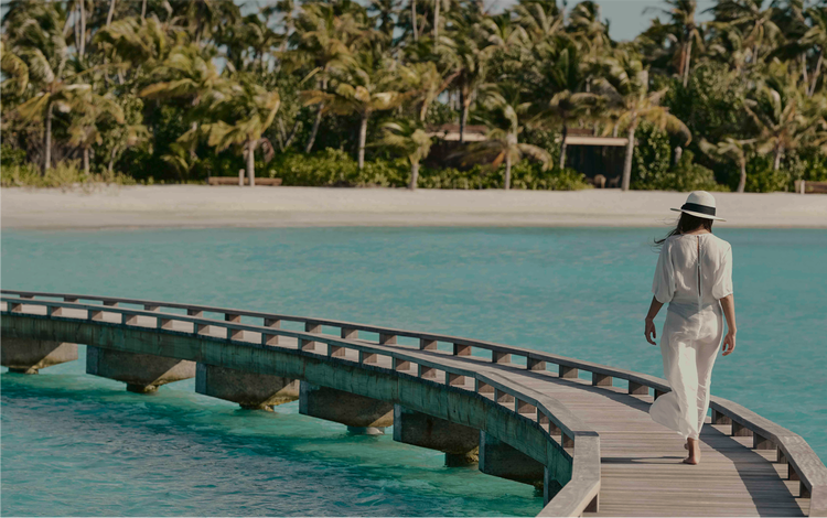 Woman walks boardwalk over turquoise lagoon.