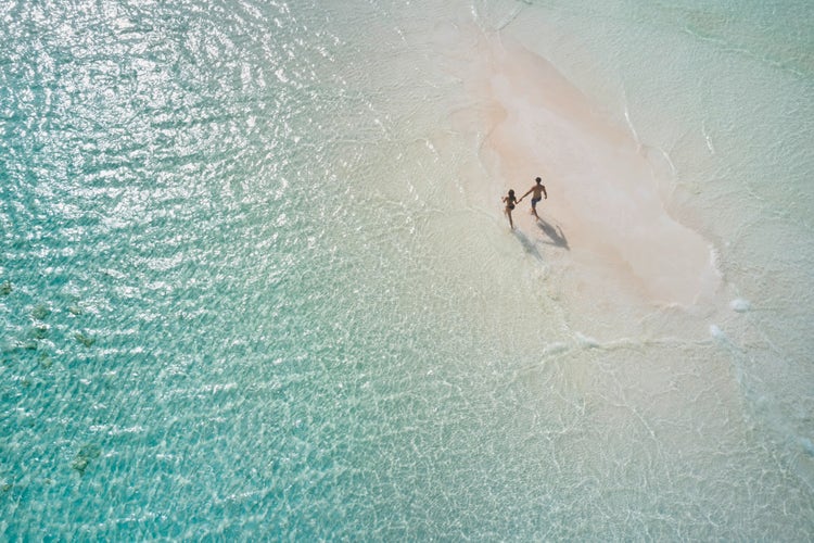 Couple walks on isolated sandbar.