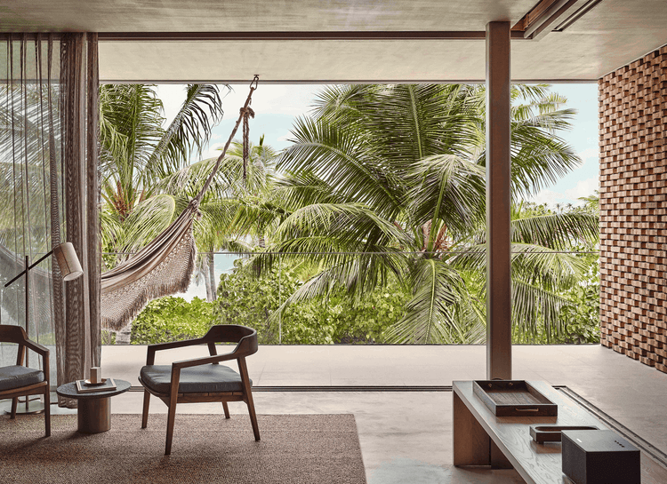 Indoor chairs face lush tropical view.