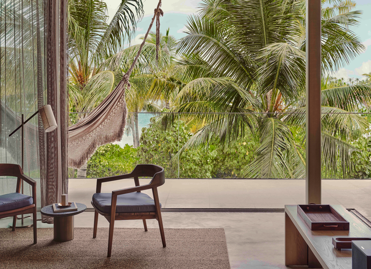 Indoor chairs face lush tropical view.