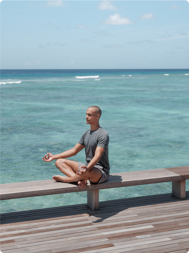 Person meditates beside turquoise ocean.