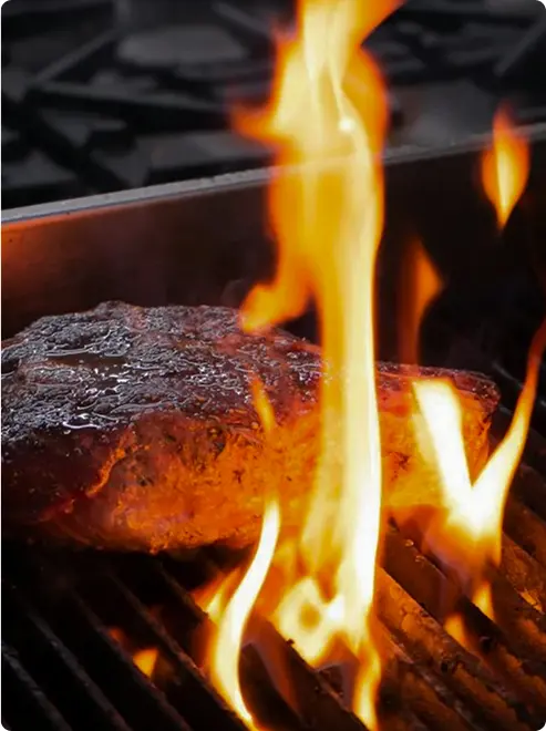 Flames rise around seared steak cut.