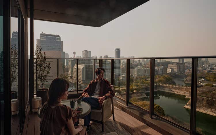 Guests relax on balcony above cityscape.
