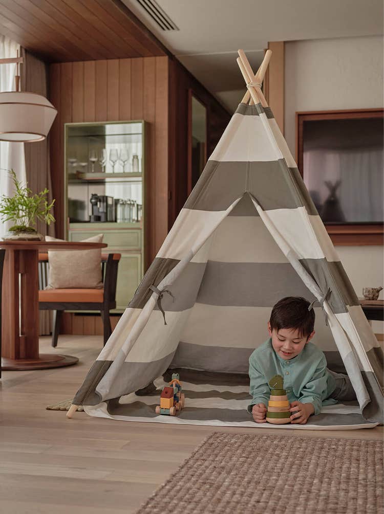 Child plays with wooden toys in teepee.