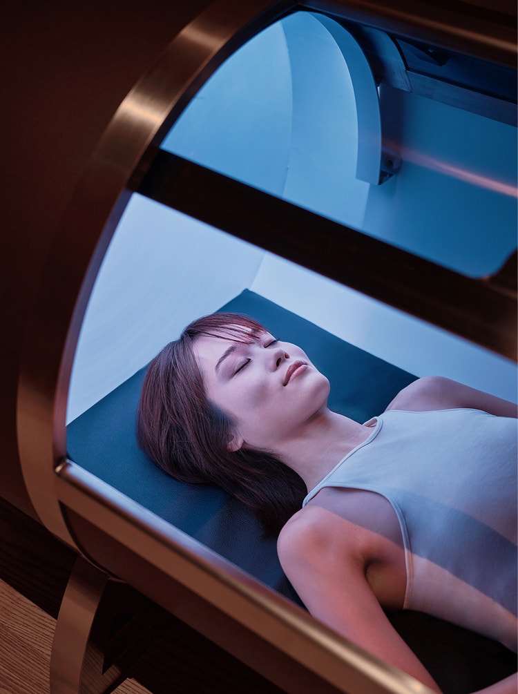 Guest reclines in illuminated therapy chamber.